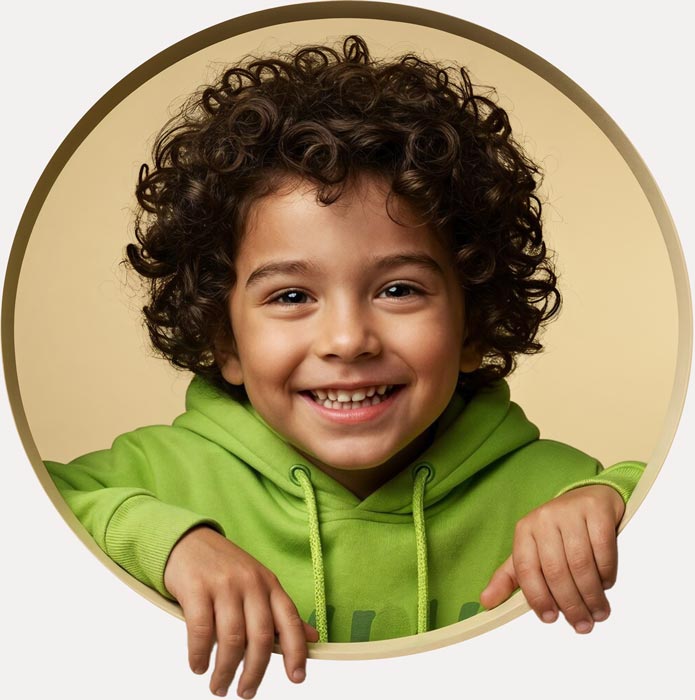 Curly-haired child in a green hoodie smiling at Krish Elite play school in ECIL
