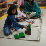Two children working with green wooden blocks on a mat
