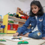 Girl sitting beside a shelf of colourful number rods