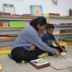 Child sitting on a rug working with wooden materials beside a classroom shelf
